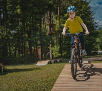 Otrok vozi po lesenem pumptracku v Pustolovskem parku NOD Završnica 